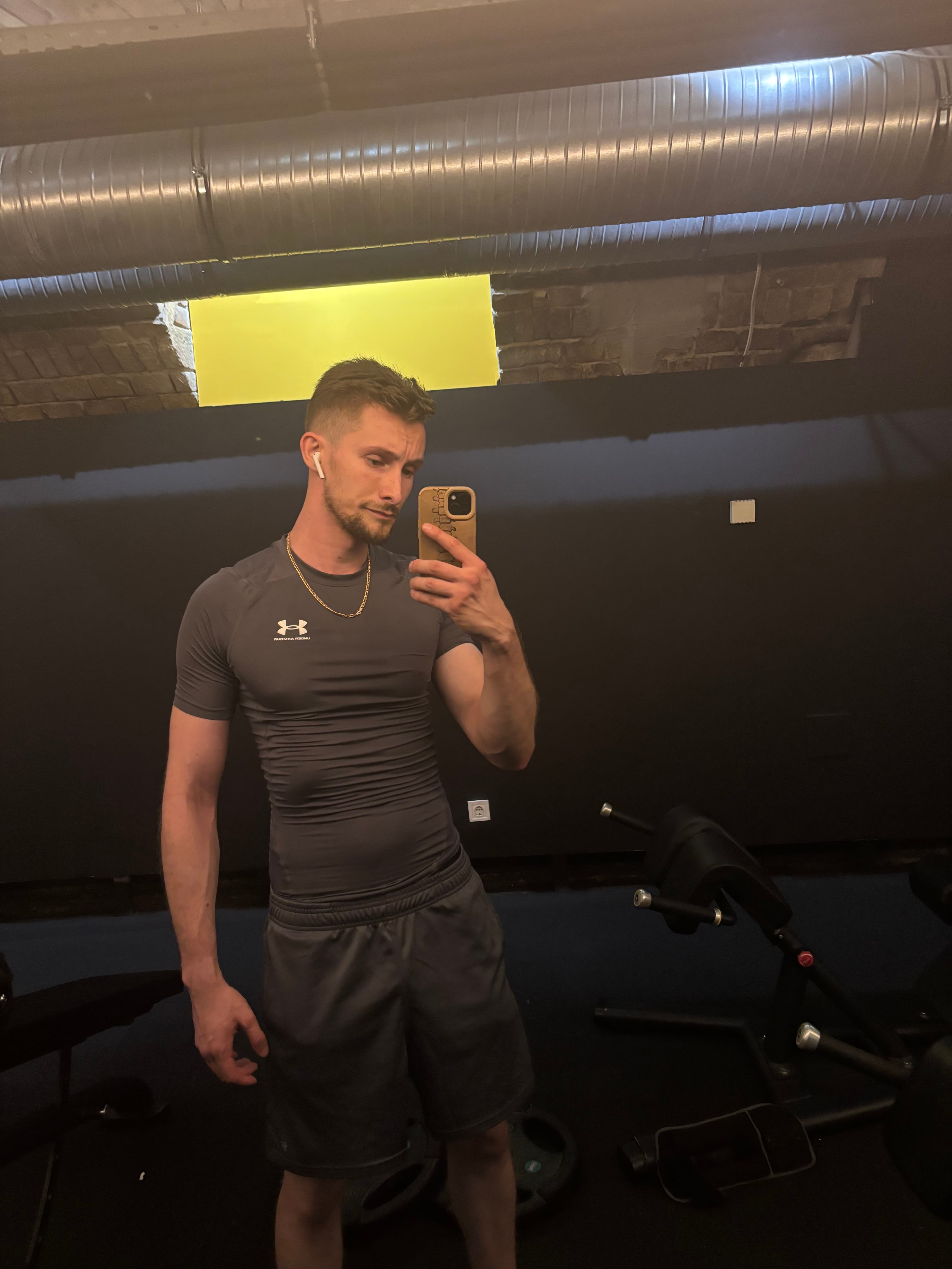 Athletic man in a grey compression shirt taking a mirror selfie in a dark gym.