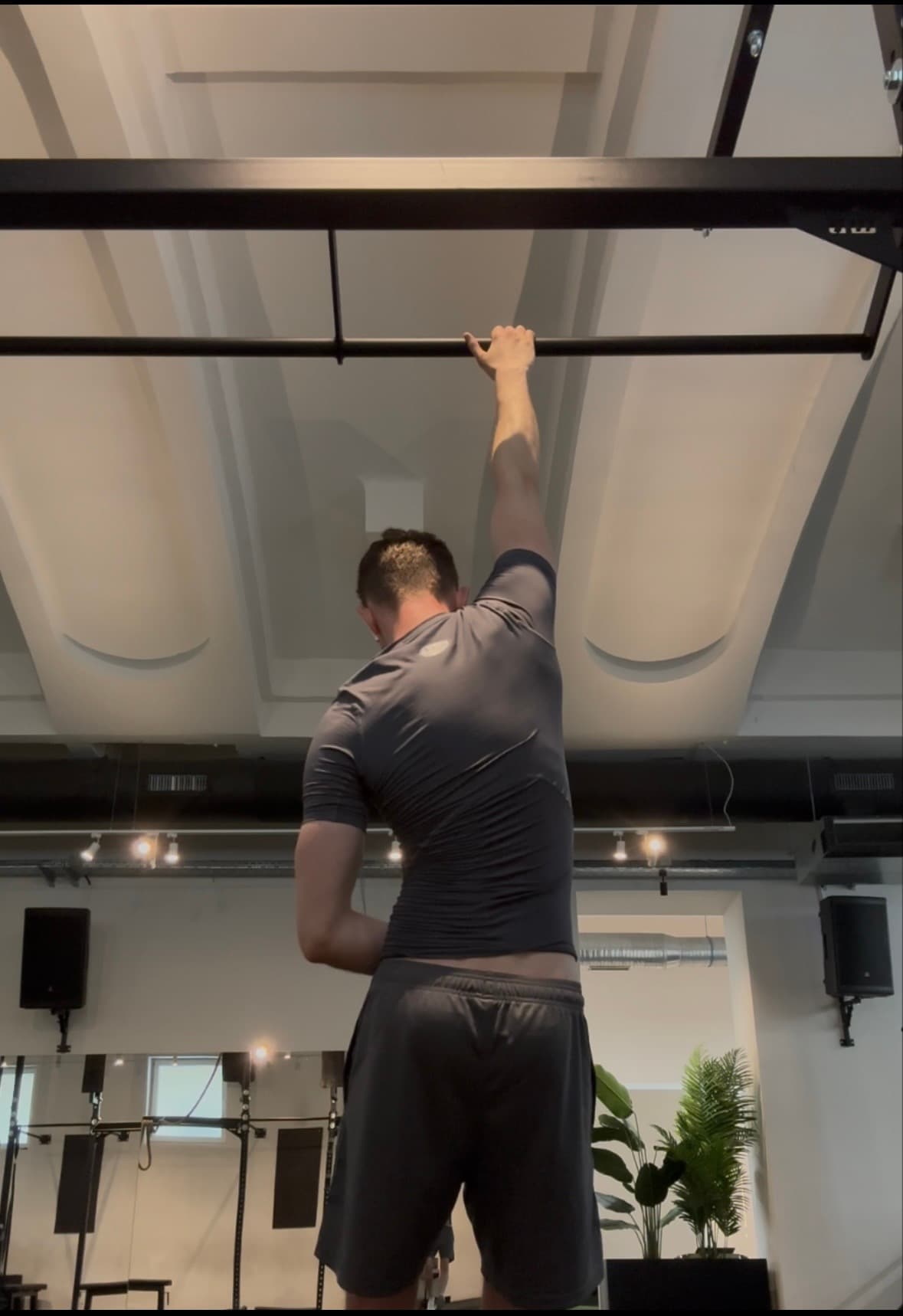 Man in a gray shirt hanging by one arm from a gym pull-up bar.